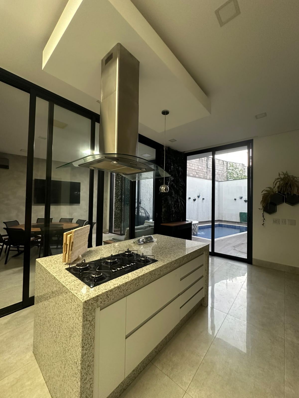 Cozinha com ilha em granito, cooktop e coifa de inox