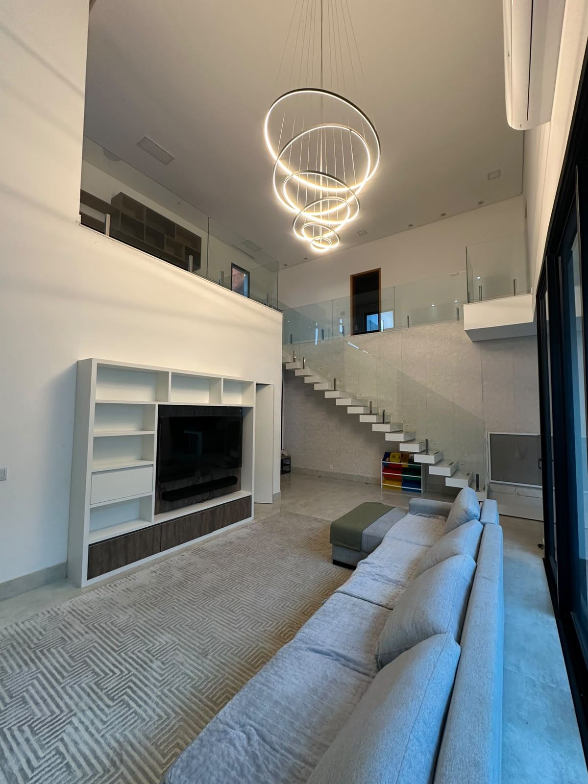Sala com pé-direito duplo, lustre de anéis e escada flutuante